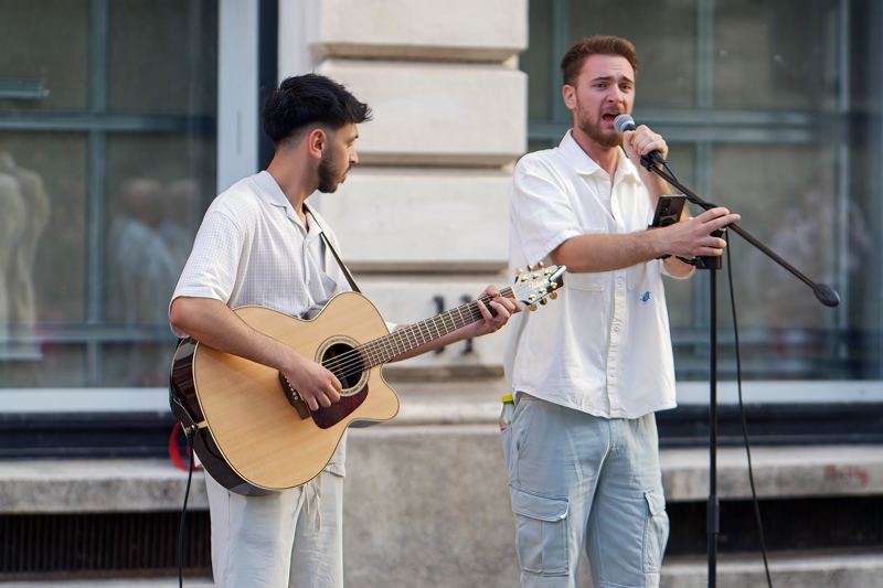coming_soon_12 - Two buskers, singing and playing an acoustic guitar on a city street